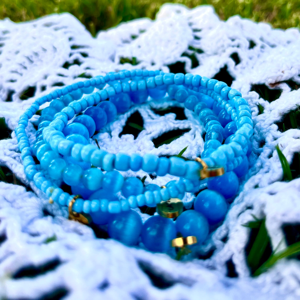 Coastal Blue Bliss blue beaded bracelet stack with gold-tone accents on a white crocheted blanket outdoors.